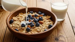 Bowl of whole grain cereal with fresh blueberries and sliced almonds on wooden breakfast table with milk
